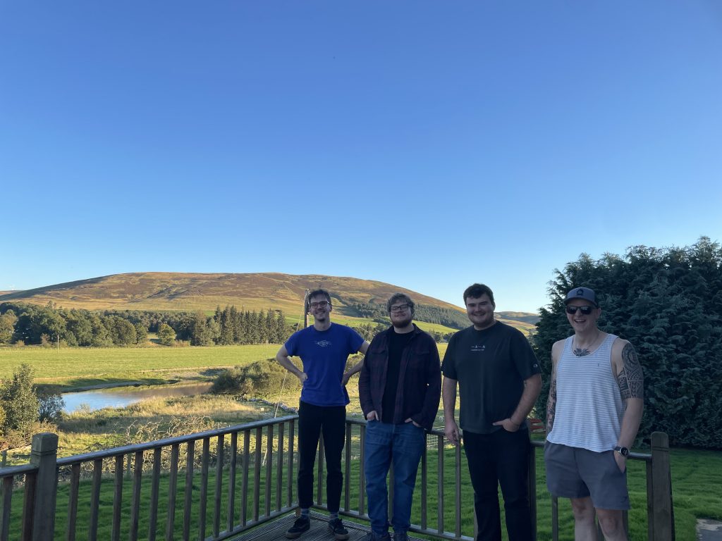 Musicians standing on a balcony at Gran's House Studio with a backdrop of fields, water, trees and hills.
