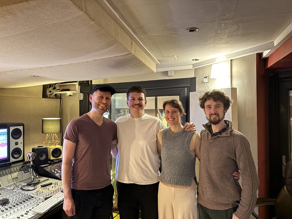 Lucie Hendy stands in a recording studio with the recording engineer and two musicians who performed on her album.